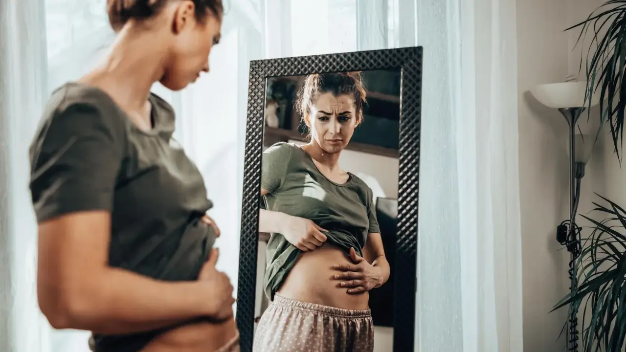 Kobieta zmartwiona dotyka brzucha, zastanawiając się, czy przy menopauzie boli brzuch.