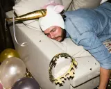 Mężczyzna w stroju jednorożca śpi na kanapie po imprezie. Balony i konfetti sugerują, że to może być sposób na to, jak pozbyć się kaca.