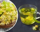 Koszyk pełen kwiatów lipy obok szklanki aromatycznej herbaty z lipy.