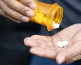 Dłoń wysypuje białe tabletki z pomarańczowego pojemnika. Czy to oxycodone? Co to jest i jak działa?