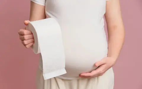 Brzuch kobiety w ciąży, trzymającej rolkę papieru toaletowego. Niestety, biegunka w ciąży to częsty problem.