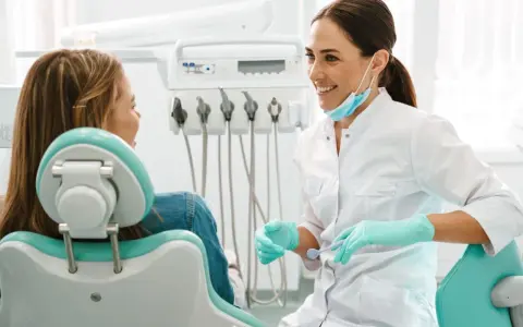 Uśmiechnięta dentystka w rękawiczkach rozmawia z pacjentką. Może właśnie omawia antybiotyk na zęba.