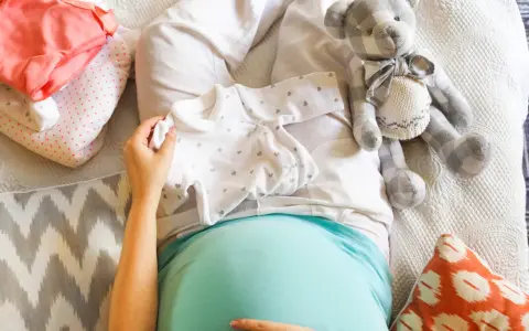 Brzuszek w 34 tyg ciąży, przygotowania do porodu. Ubranka dla maluszka, pluszowy miś i poduszki.