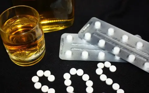Szklanka alkoholu i blistry z tabletkami układają się w napis SOS. Czy to pytanie o benzodiazepiny, co to jest i jakie ryzyko niesie ich połączenie z alkoholem?
