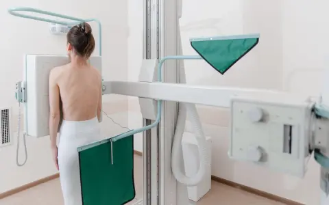 Kobieta przygotowuje się do badania RTG klatki piersiowej. Aparatura medyczna jest gotowa do wykonania zdjęcia.