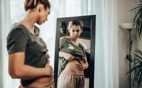 Kobieta zmartwiona dotyka brzucha, zastanawiając się, czy przy menopauzie boli brzuch.