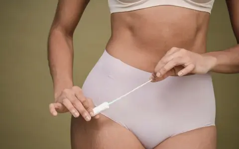 Kobieta trzymająca tampon, zastanawiająca się, czy okres się spóźnia.