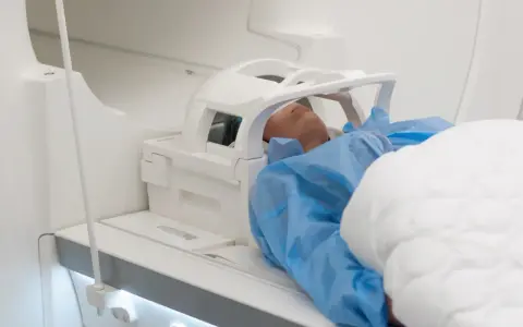 Pacjent w niebieskim fartuchu leży w aparacie MRI, przygotowany do badania głowy. Może to być związane z podejrzeniem nieprawidłowego rezonansu głowy.