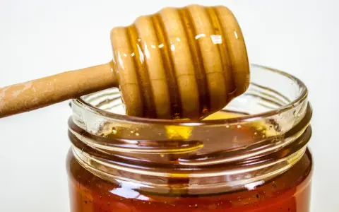 Słoik z miodem i drewniana łyżka do miodu. Naturalny antybiotyk na gardło, który pomoże złagodzić ból.
