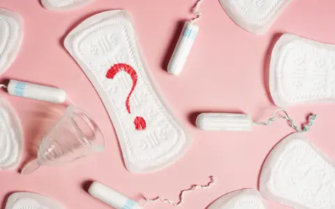 Pytajnik z krwi na podpaskach, obok tampony i kubeczek menstruacyjny. Czy to plamienie przed okresem?