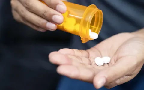 Dłoń wysypuje białe tabletki z pomarańczowego pojemnika. Czy to oxycodone? Co to jest i jak działa?