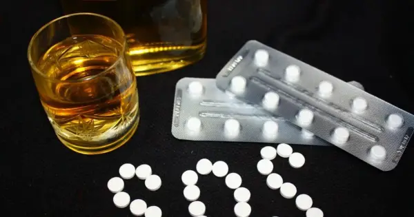 Szklanka alkoholu i blistry z tabletkami układają się w napis SOS. Czy to pytanie o benzodiazepiny, co to jest i jakie ryzyko niesie ich połączenie z alkoholem?