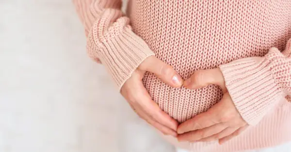 Dłonie tworzą serce na brzuchu ciężarnej. Warto pamiętać, że żółte upławy w ciąży mogą być sygnałem do konsultacji z lekarzem.
